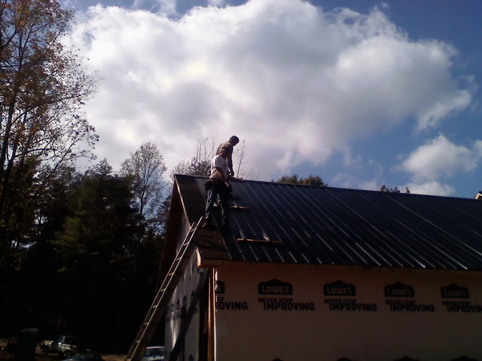 Roofer fastening dark metal panels high against a cloudy sky, from a Roof Inspection job in South Cle Elum