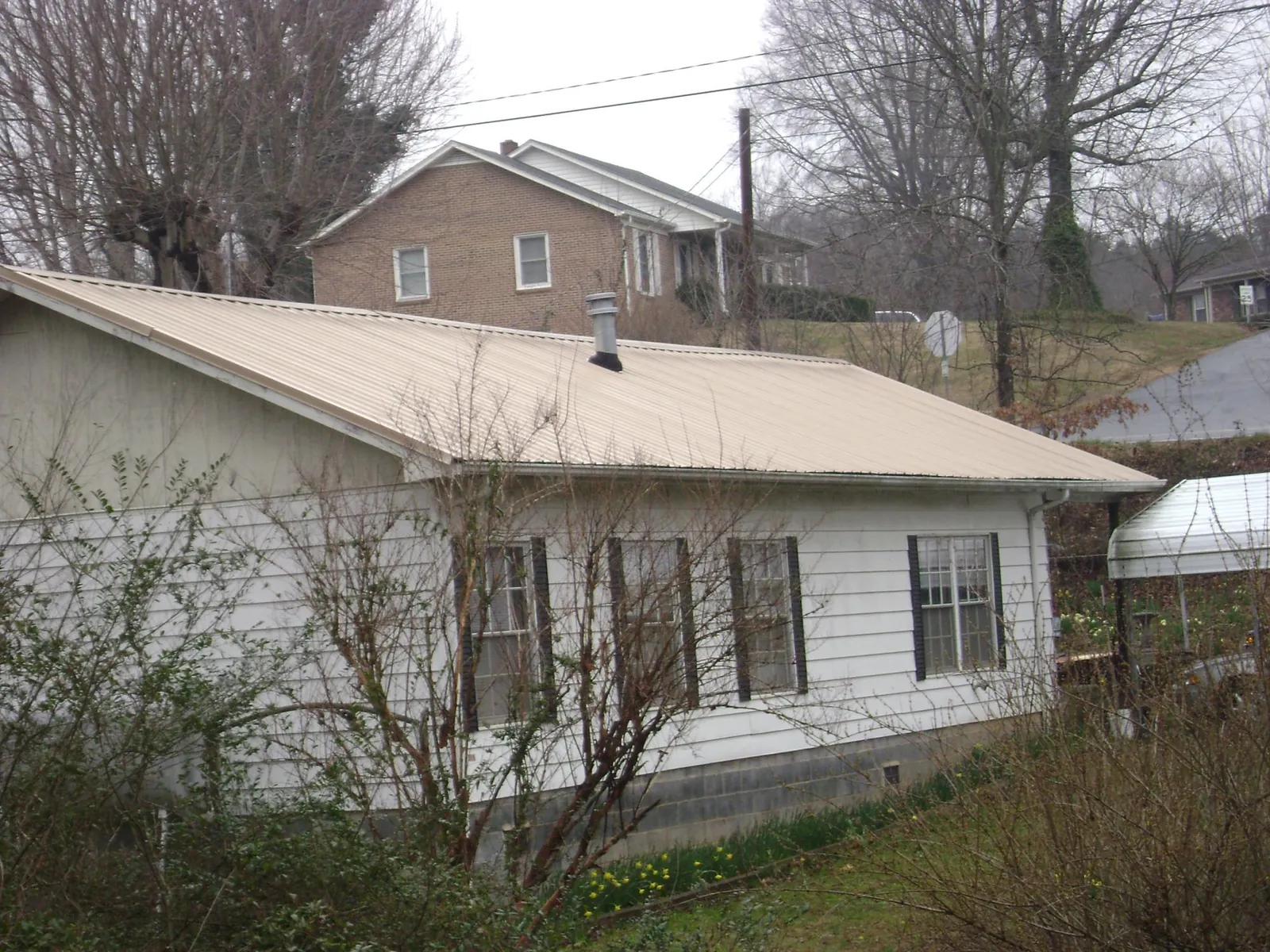 Tan metal roof on a white sided house set into a hillside — Commercial Roofing by Roofing Brothers in South Cle Elum
